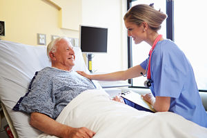 A nurse is sitting on the bedside of a patient with her hand on his shoulder