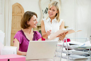 A Management team member is speaking to another about a file while one is typing on a laptop.